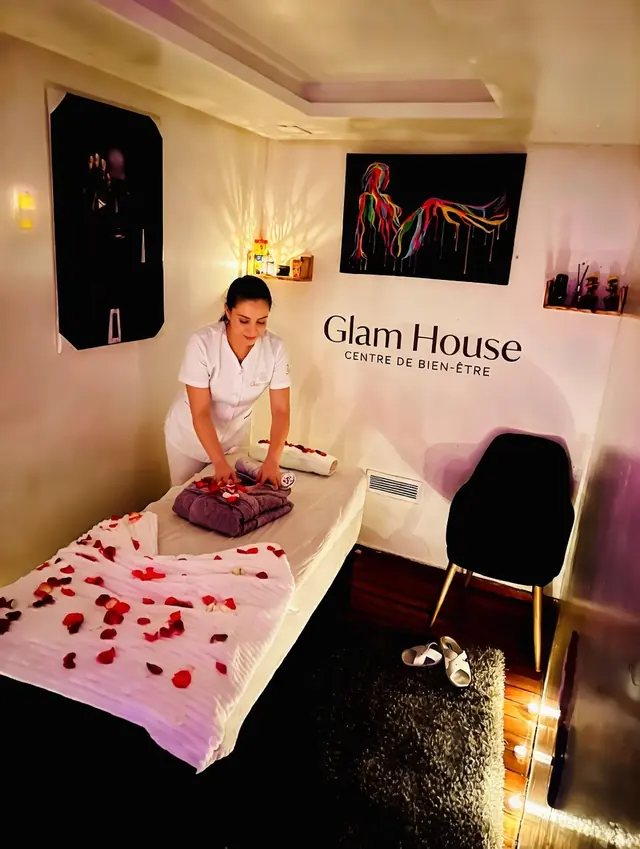 Thérapeute Glam House Casa préparant un peignoir et des pétales de rose sur la table de soin